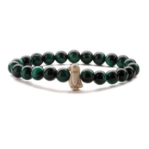 Detailed view of green tiger eye beads and a white penguin charm on elastic bracelet