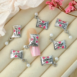 Macro shot of silver metal nail charm with Sweet text, pink heart and white pearl drop