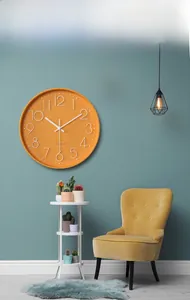 Modern orange wall clock with 3D white numerals on a blue wall in a living room