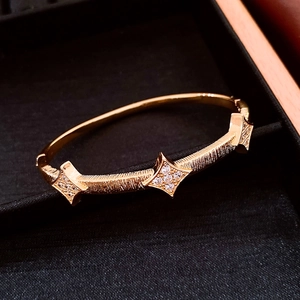 Macro detail of 18K gold plated bangle with starburst motifs and brushed metal texture