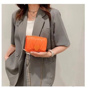 Detail of vibrant orange mini crossbody bag featuring heart-shaped buckle and V-quilted pattern