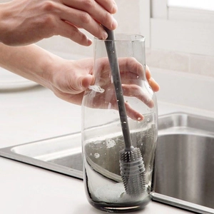 Long-handle silicone cleaning brush scrubbing a transparent glass bottle in a kitchen sink