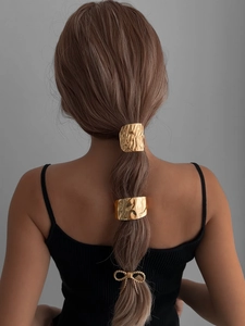 Detailed view of golden hammered metal hair ring and bow accessories on model ponytail