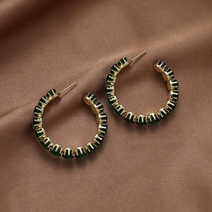 Detailed close-up of C-shaped gold hoops featuring emerald green baguette gemstones on silk