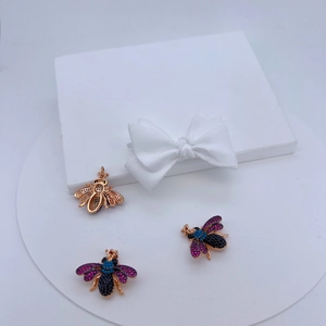 Macro detail of three bee-shaped insect pendants with zircon inlays and gold plating