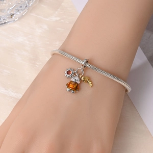 Detailed shot of a bear charm on a silver snake chain bracelet with autumn-themed accents