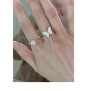 Detailed close-up of gold butterfly and pearl rings on model's finger, vintage style