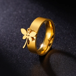 Golden wide band stainless steel ring featuring a delicate dragonfly charm on a black background