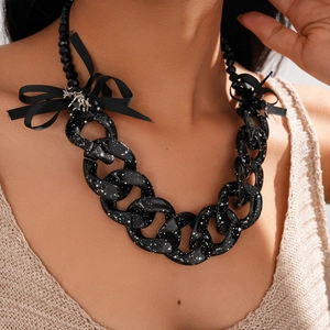 Close-up of black acrylic chain necklace with white paint splatter and ribbon bow