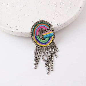Close-up of rainbow woven letter G brooch featuring sparkling rhinestone fringe detail