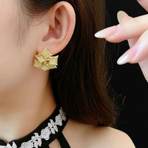 Close-up of vintage style gold-rimmed cream square earrings worn by a model