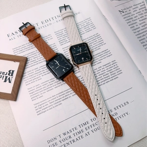 Close-up of minimalist square quartz watches with brown and white leather bands on a book