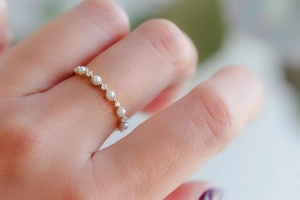 Macro detail of a thin gold ring with white pearls worn on a finger in soft focus