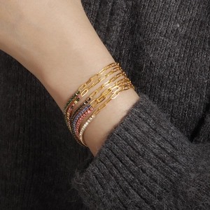 Close-up of layered gold bracelets with colorful zirconia on a gray knit sweater