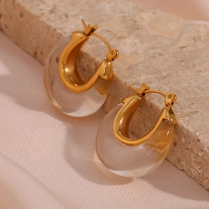 Detail of U-shaped gold earrings with transparent resin on a beige stone and pink fabric