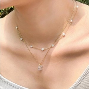 Close-up of double-layer gold necklace featuring white pearls and a crystal lock pendant