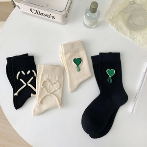 Dettaglio di calze con ricamo a cuore e nappe su sfondo bianco minimalista