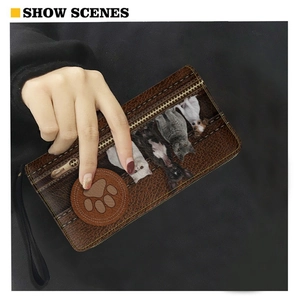 Brown long zipper wallet with cat print and paw detail held in hand on black background