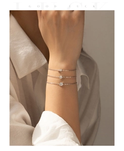 Three stacked sterling silver bracelets with round moissanite charms on female wrist