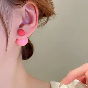 Double-sided ball stud earrings in red and pink resin finish worn by a model