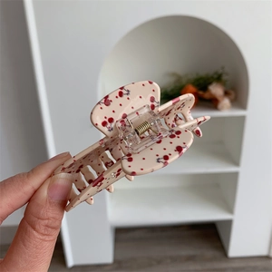 Detail of floral acetate hair claw clip featuring red cherry pattern on beige base