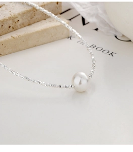 Detalle de collar en plata 925 con colgante de perla blanca sobre fondo de un libro