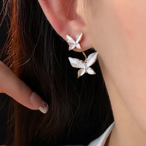 Élégantes boucles d'oreilles double papillon dorées avec émail blanc sur un mannequin