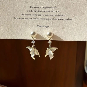 Detailed macro view of wing-shaped pearl earrings with gold edging on a quote card