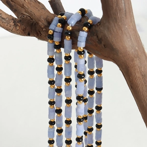 Collier fait main avec pierres bleu clair, perles dorées et noirs sur une branche