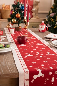 Detail of red jacquard Christmas table runner with reindeer motifs on a wooden table