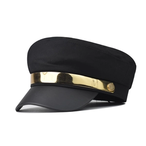 Detailed close-up of newsboy cap with gold metal band and decorative letter M engraving