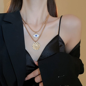 Detail of layered gold double chain necklace with evil eye charm and hammered coin pendant