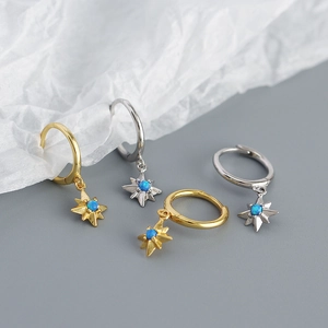 Macro shot of gold and silver starburst earrings with blue opal stone on white paper