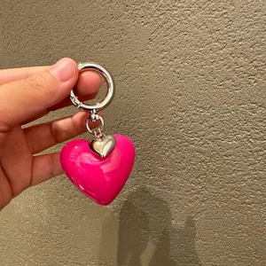 Pink heart keychain charm with silver metal accents held against a textured wall