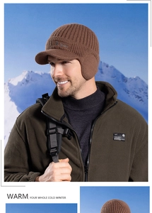 Close-up of brown knit winter hat with ear flaps and fleece jacket on snow mountain