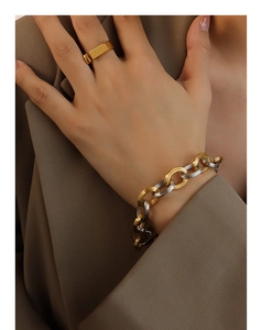 Detail of two-tone chain bracelet and wide gold ring worn with a beige blazer suit