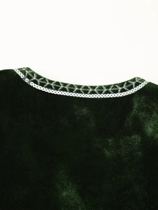 Macro detail of dark green velvet vest featuring intricate gold embroidery and sequins