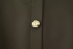 Détail d'un bouton en métal doré texturé sur le tissu de robe vert olive foncé