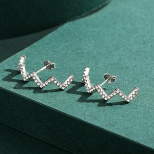 S925 sterling silver wave drop earrings with cubic zirconia pavé on green background