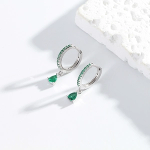 Detail view of silver earrings featuring green teardrop pendants on textured stone