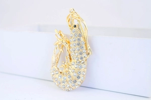 Detailed side view of a gold lobster brooch with sparkling rhinestones on a white box