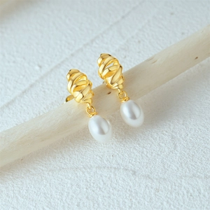 Detail of twisted gold earrings with white drop pearls hanging on a wooden branch