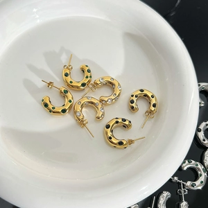 Close-up of gold C-shaped earrings with irregular texture and colored zircon stones