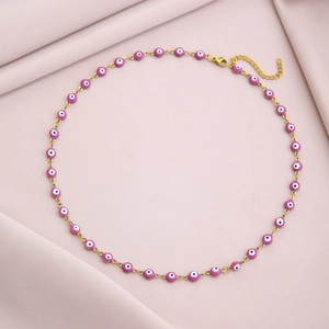 Detail of gold chain necklace with pink evil eye beads on soft pink fabric background