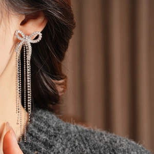 Close-up of 18k gold plated bow earrings with zircon tassels on a female model