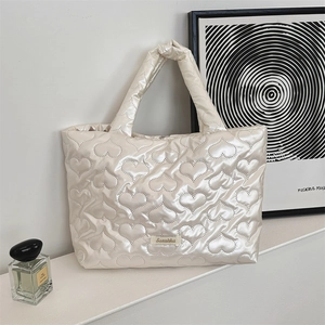 Detail of heart-quilted texture on a pearl white puffer tote bag with brand label