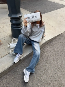 Detail of a dark grey half-zip sweatshirt and blue wide-leg jeans in a street style look