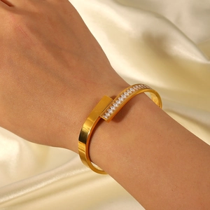 Gros plan d'un bracelet jonc en acier plaqué or 18K avec zircons posé sur de la soie