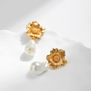 Goldene Blumenohrringe mit Barockperlen auf weißem strukturiertem Hintergrund