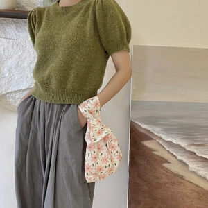 Wristlet pouch featuring pink floral patterns worn with a green knit short sleeve sweater